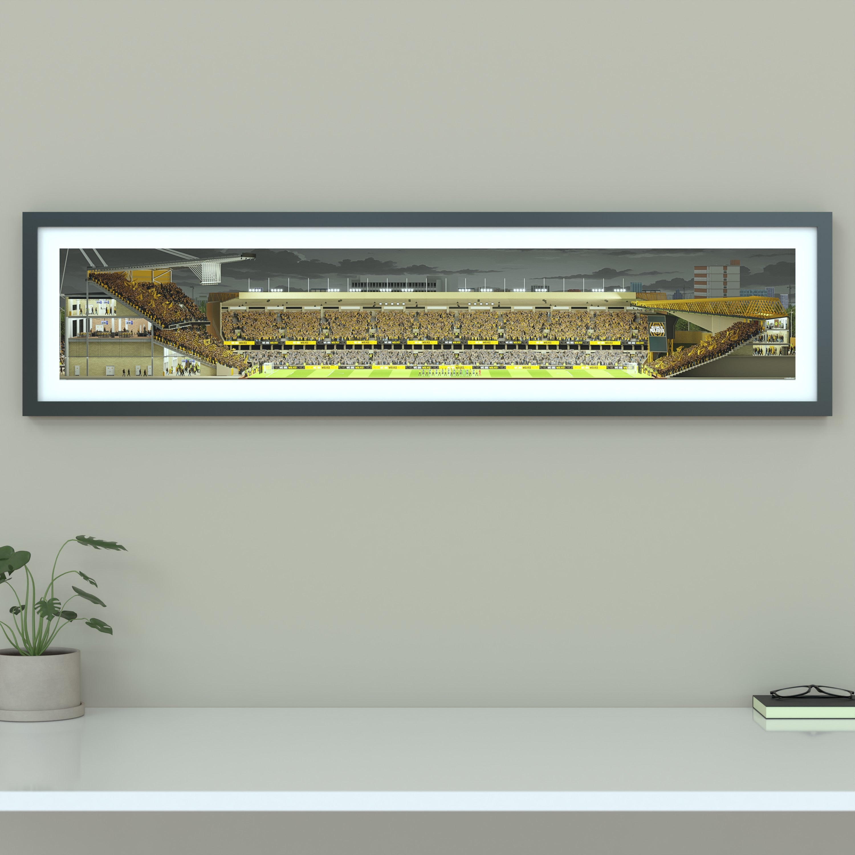 A framed panoramic art print of a Wolves' Molineux stadium, mounted on a light gray wall. The print features a detailed illustration of a stadium filled with yellow and black clad fans under a dark sky.