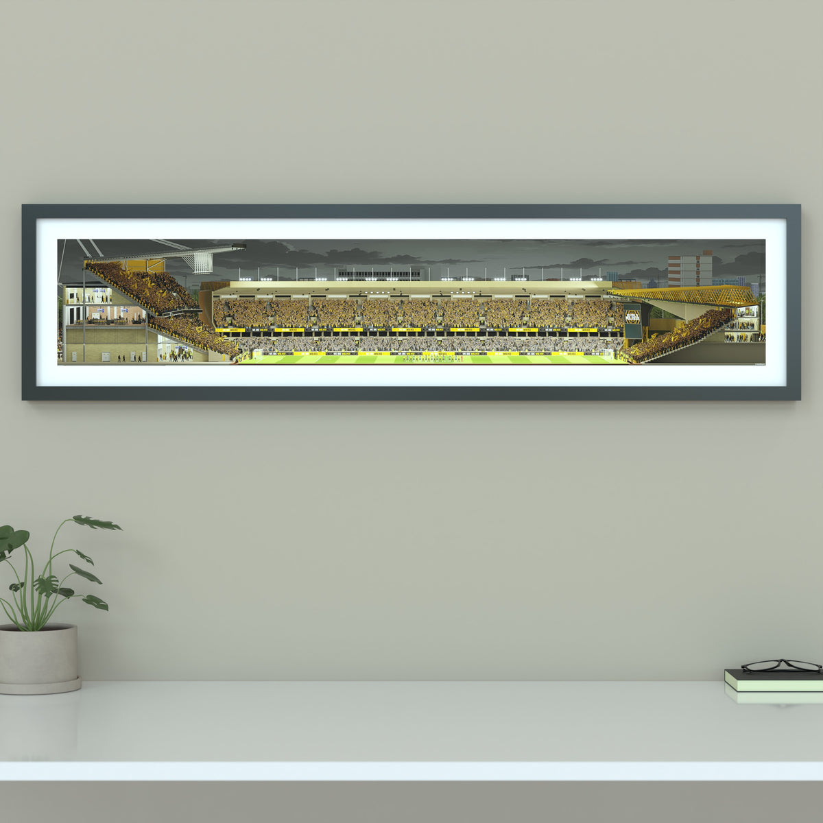 A framed panoramic art print of a Wolves' Molineux stadium, mounted on a light gray wall. The print features a detailed illustration of a stadium filled with yellow and black clad fans under a dark sky.